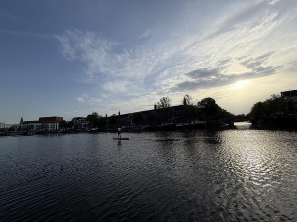 A lone paddleboarder glides across the tranquil waters of the Amstel in Centrum, Amsterdam, under a beautiful golden hour sky